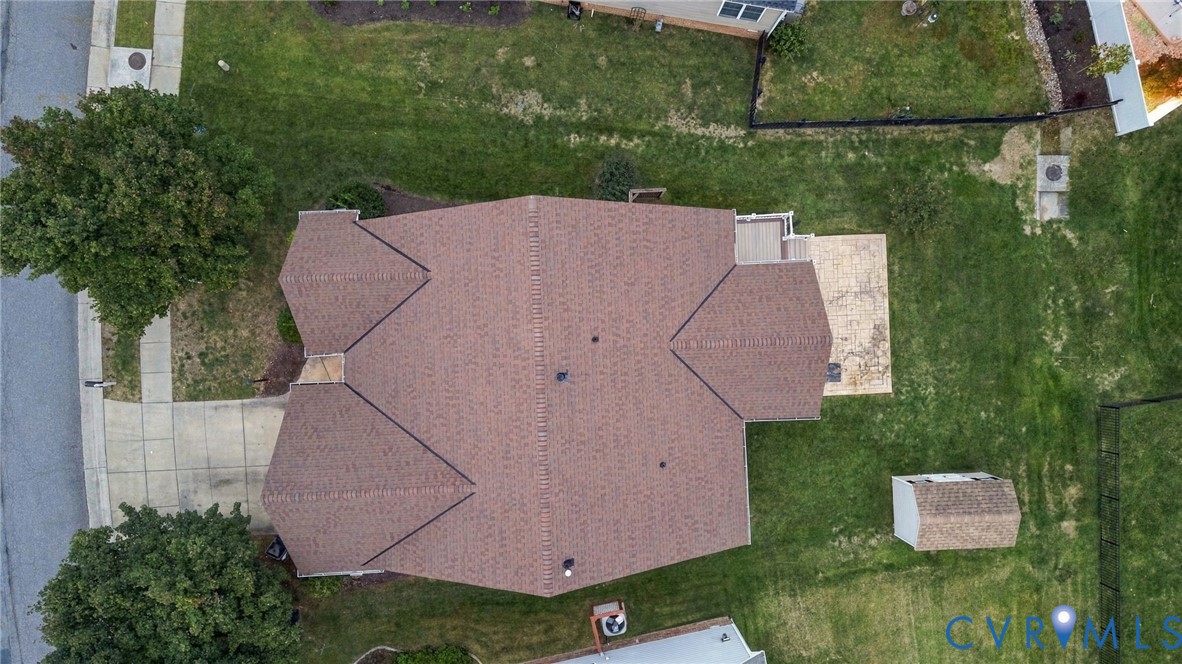 Pitched roof with asphalt shingles, expansive lawn, concrete patio, and detached storage shed