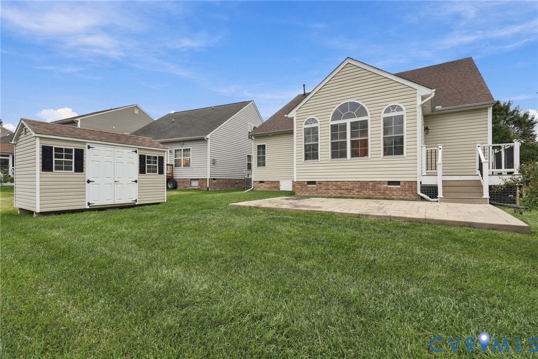 Expansive lawn featuring a stamped concrete patio, deck with railings, and storage shed with double doors