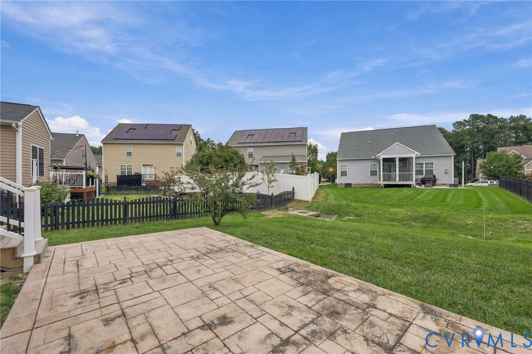 Expansive green space featuring a stamped concrete patio, a white vinyl fence, and a black picket fence