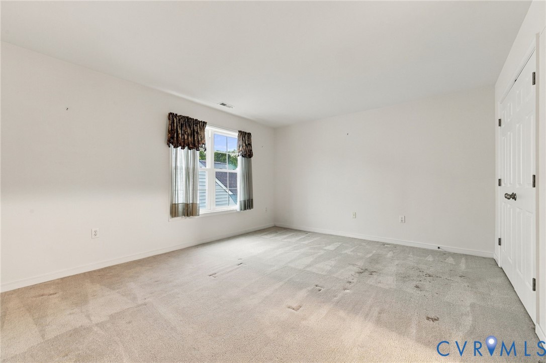 Bright, spacious bedroom showcasing neutral wall finishes, abundant natural light from dual windows, and neutral-toned carpet flooring