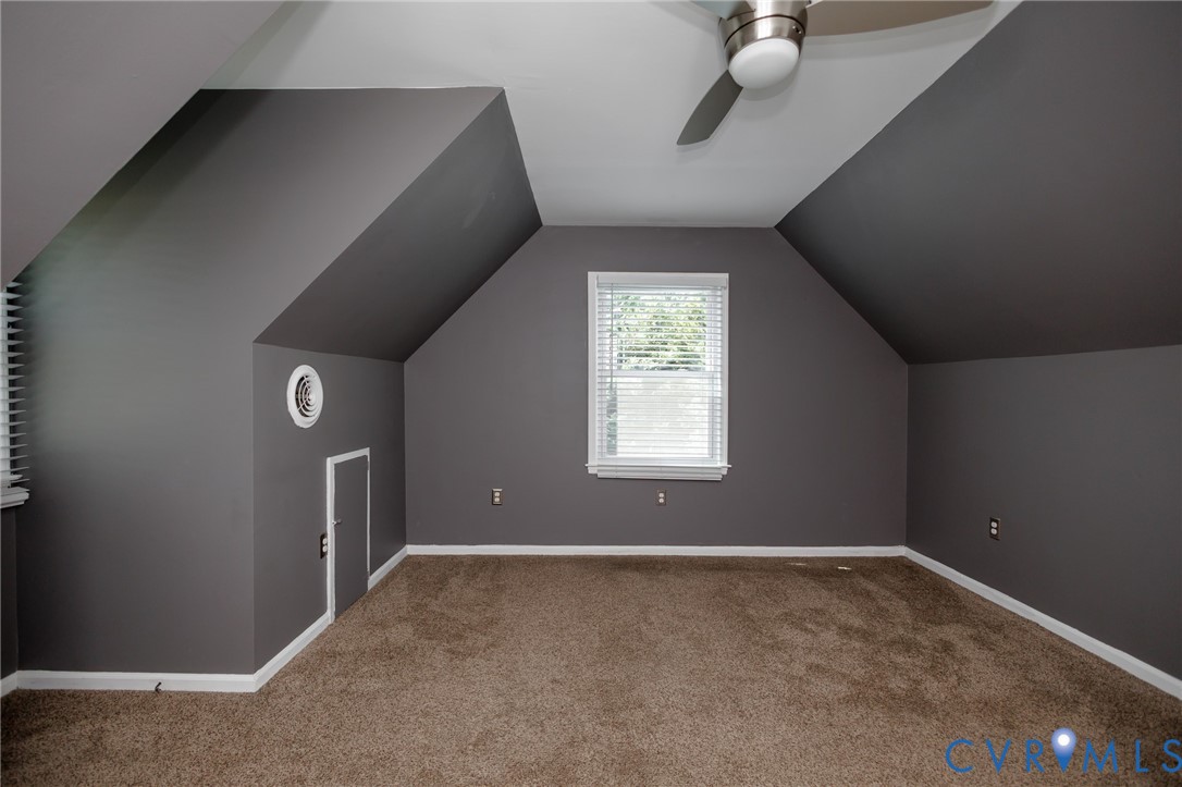 Carpeted room with sloped ceilings, a window with blinds, and a ceiling fan