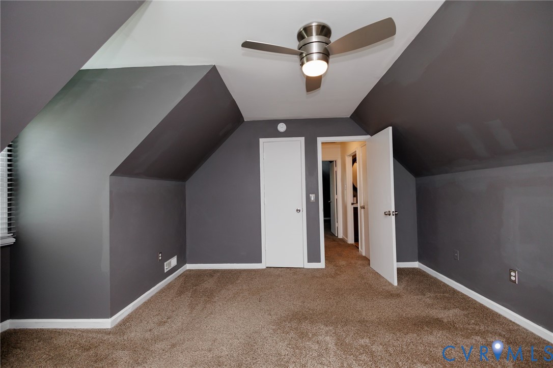 Angled ceiling with a contemporary ceiling fan, plush carpet, white trim, and a white door with brushed nickel hardware