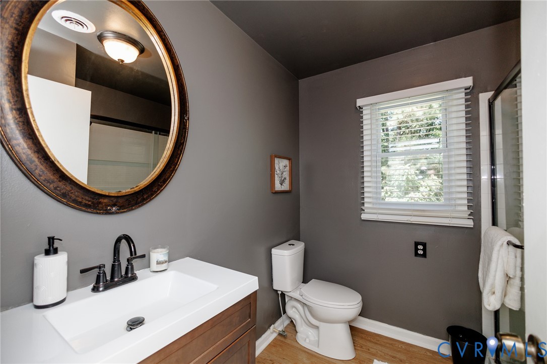 Bathroom featuring a wood-finish vanity with a white countertop, an oval mirror, a window with blinds, and wood-finish flooring