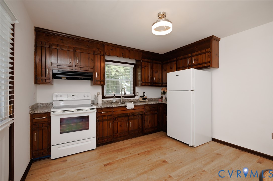 Kitchen featuring abundant wood cabinetry, light-toned wood-finish flooring, and white appliances