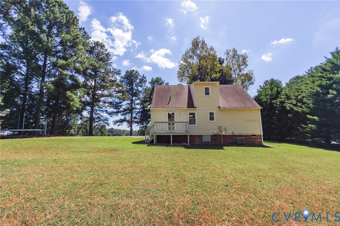Expansive grassy yard with a deck, surrounded by mature trees, and featuring a siding exterior