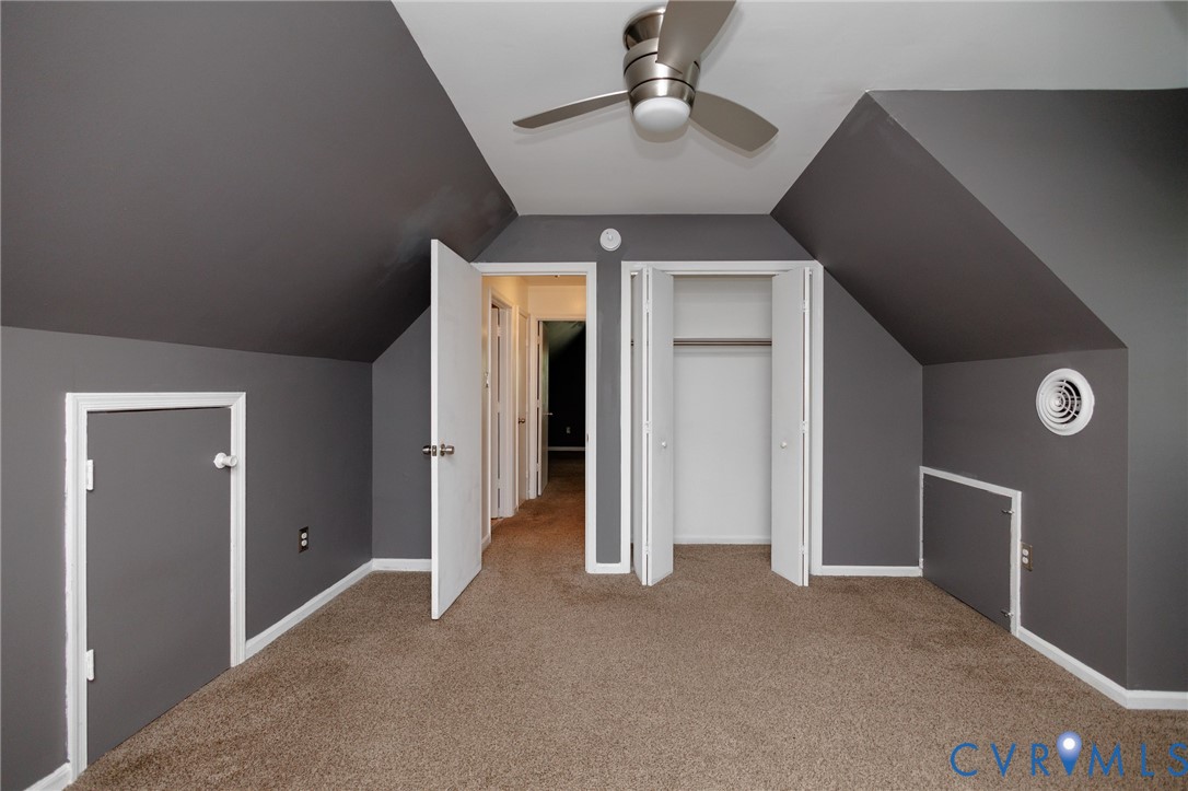 Room with sloped ceilings, plush carpet flooring, and a ceiling fan