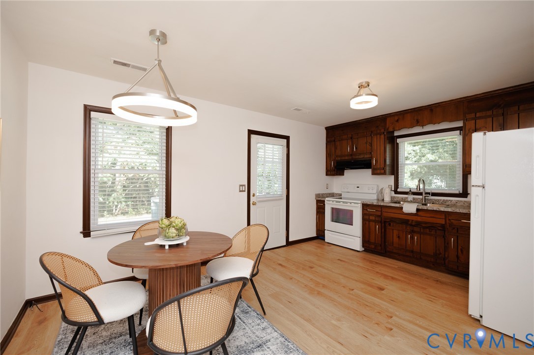 Wood-finish flooring, dark wood cabinetry, light-toned countertops, and a white appliance suite