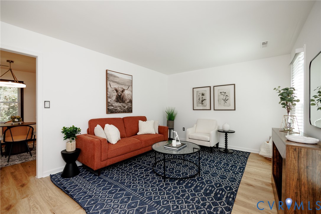 Bright living area featuring wood-finish flooring, white walls, and a visible doorway to an adjacent space