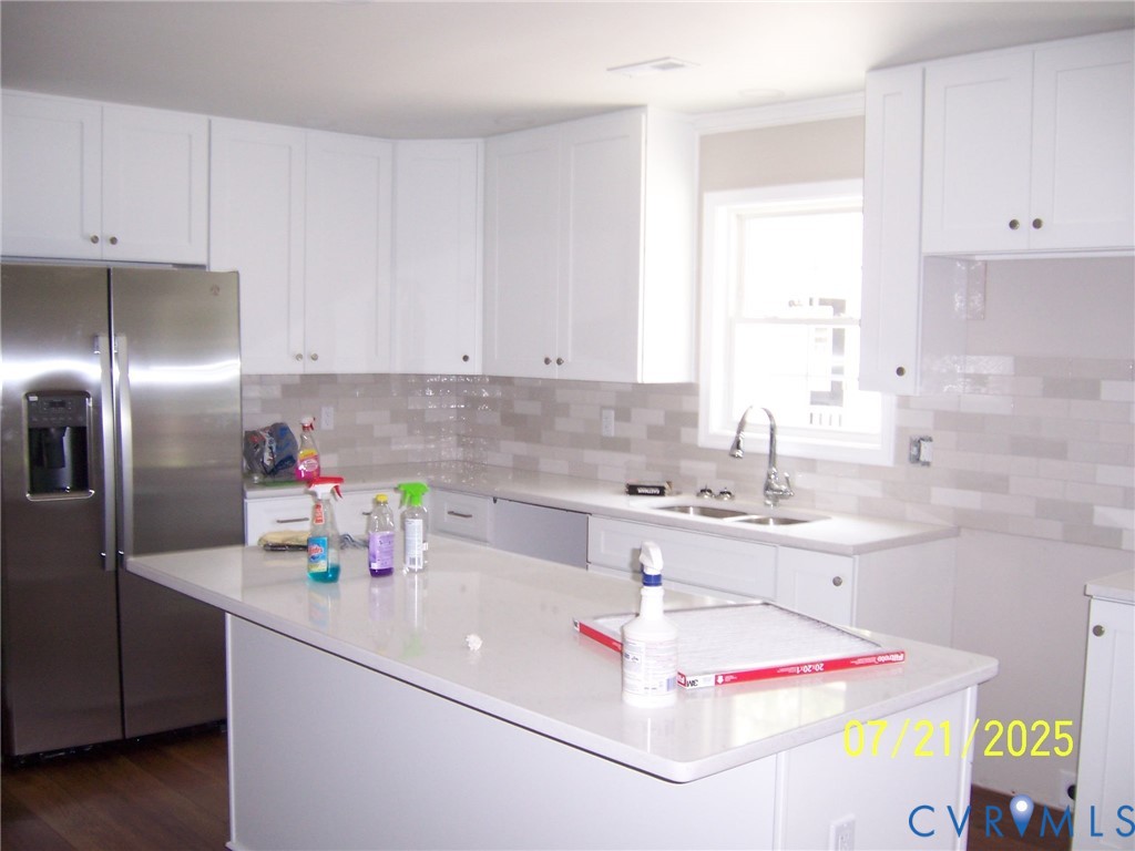 Kitchen with stainless steel fridge, white cabinets, light countertops, a kitchen island, and tasteful backsplash