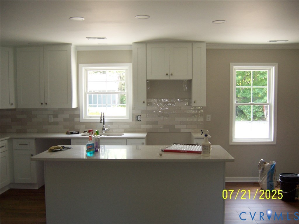 Kitchen featuring dark wood-style flooring, light countertops, a center island, decorative backsplash, and crown molding Kitchen featuring dark wood-style flooring, light countertops, a center island, decorative backsplash, and crown molding