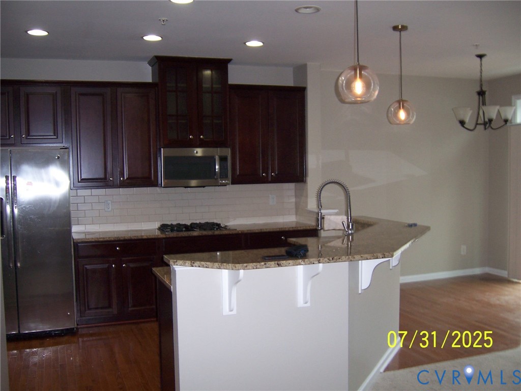 Kitchen featuring stainless steel appliances, dark wood-style flooring, a breakfast bar, decorative backsplash, and recessed lighting