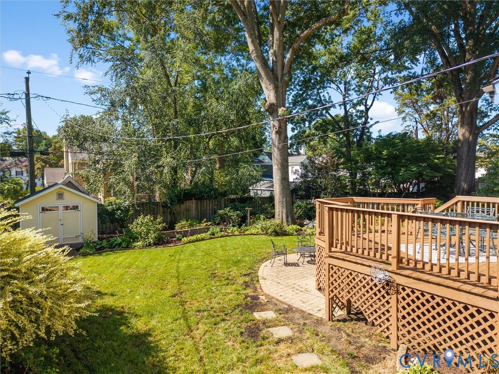 Spacious backyard featuring a multi-level wood deck, paver patio, lush lawn, mature trees, and a detached storage shed