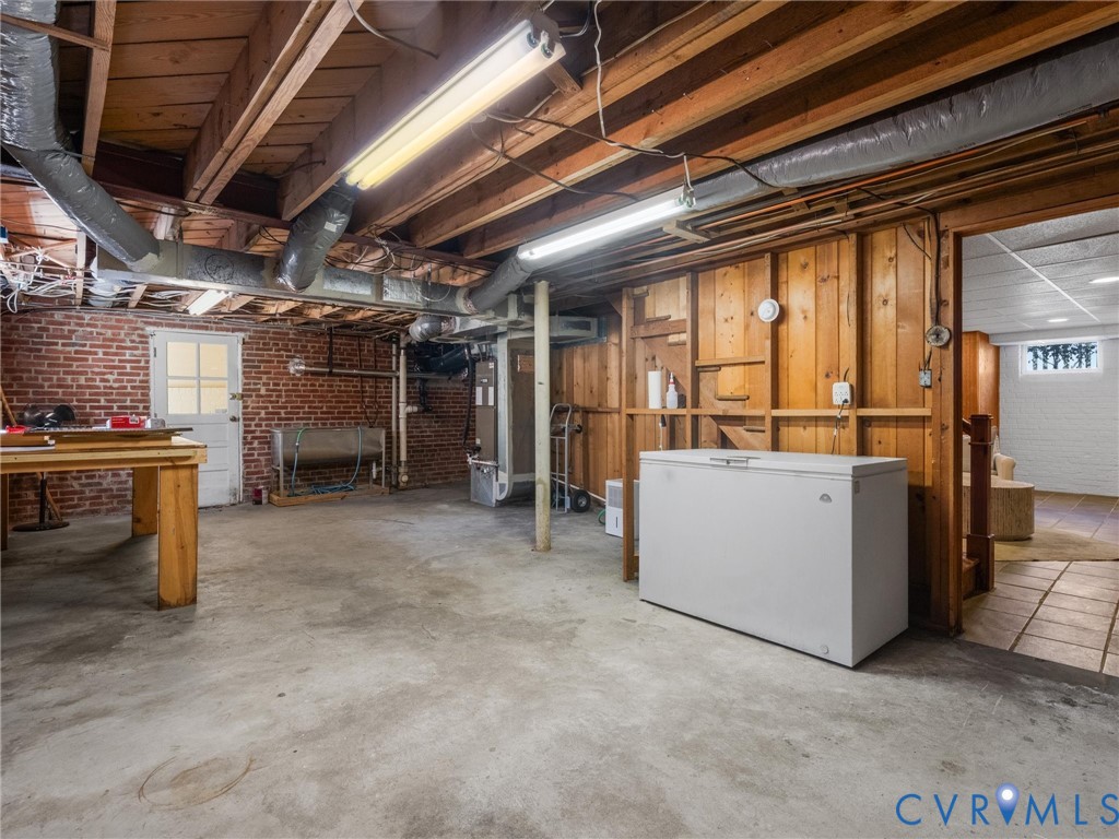 Exposed ceiling joists with ductwork, concrete flooring, brick wall accent, wood paneling, and a white paneled door