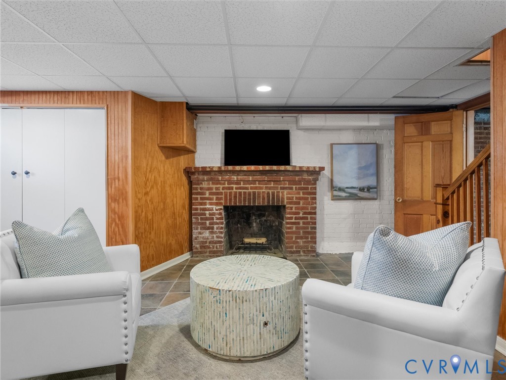 Brick fireplace with hearth, tile flooring, wood paneling, white built-in cabinetry, and wood staircase
