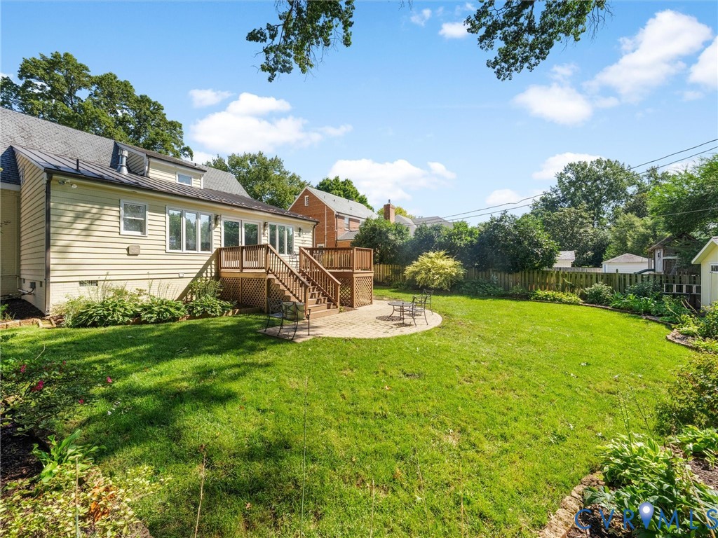 Expansive backyard featuring a lush lawn, a multi-level wood deck, a circular paver patio, and mature perimeter landscaping