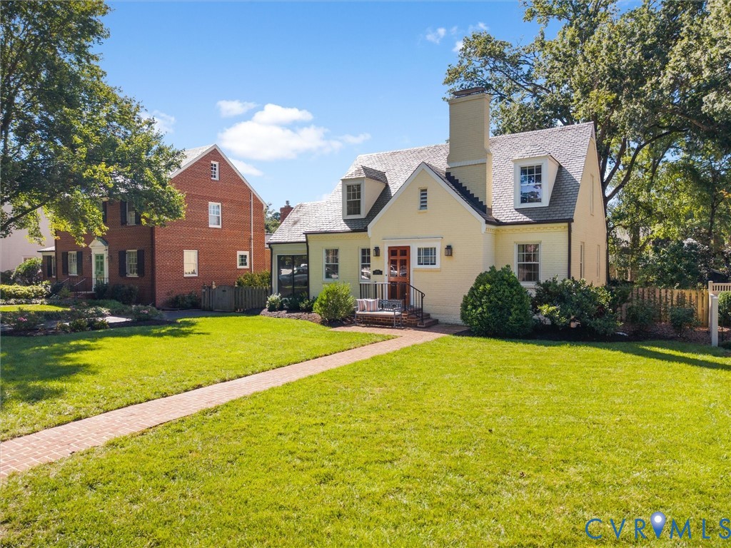 Cape Cod style residence with dormer windows, a brick pathway, and mature landscaping