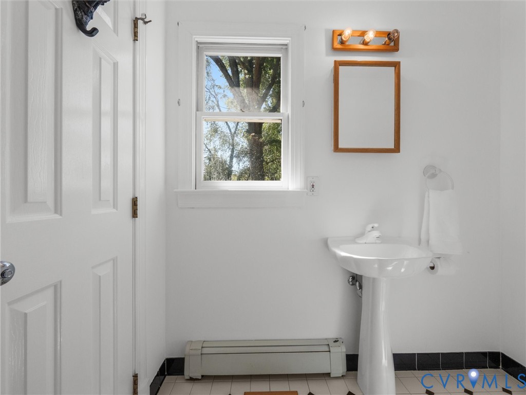 White pedestal sink, wood-framed mirror, wood-finish light fixture, white interior door, and black and white floor tiles