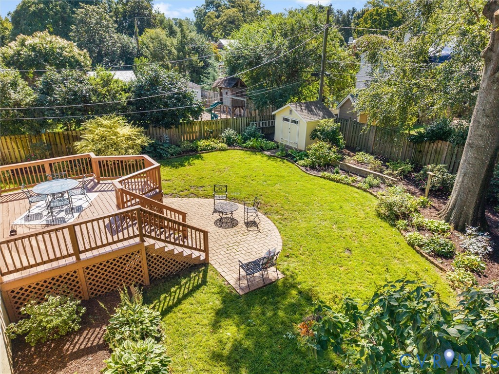 Expansive backyard featuring a multi-level wood deck, a brick paver patio, a lush lawn, established garden beds, and a storage shed