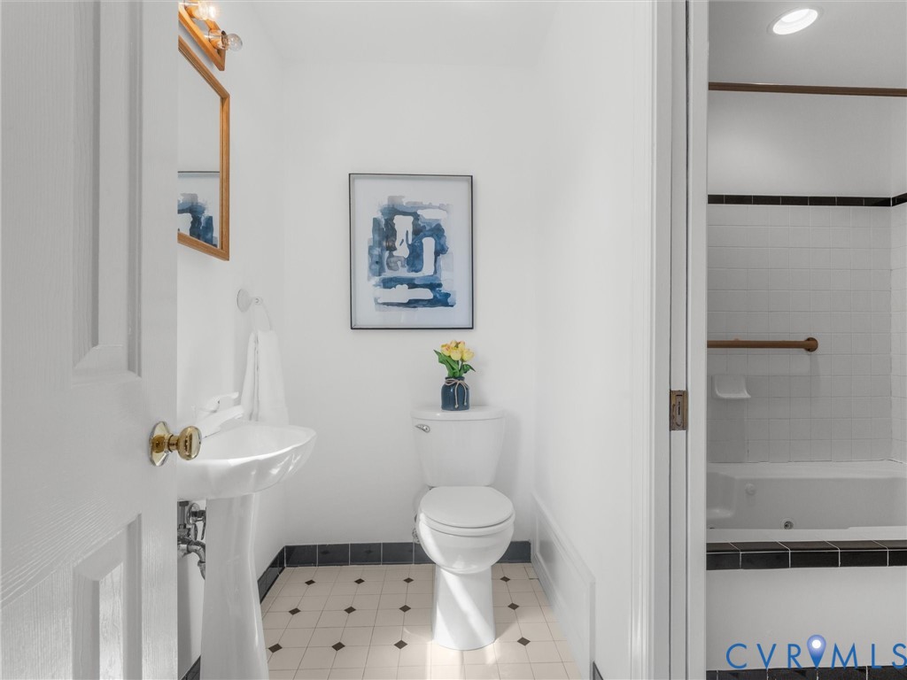 Pedestal sink, wall-mounted mirror with sconce lighting, white toilet, and black and white floor tiling