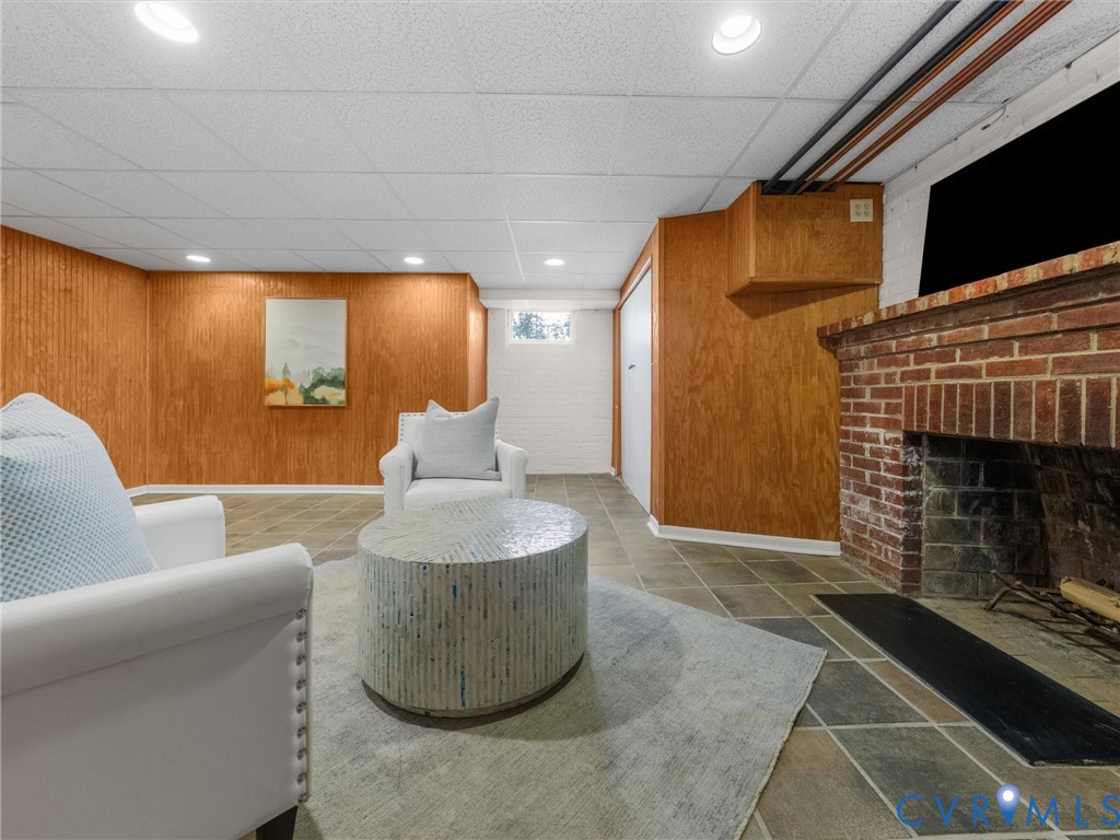Brick fireplace feature, wood-paneled walls, recessed lighting, drop ceiling, and square tile flooring