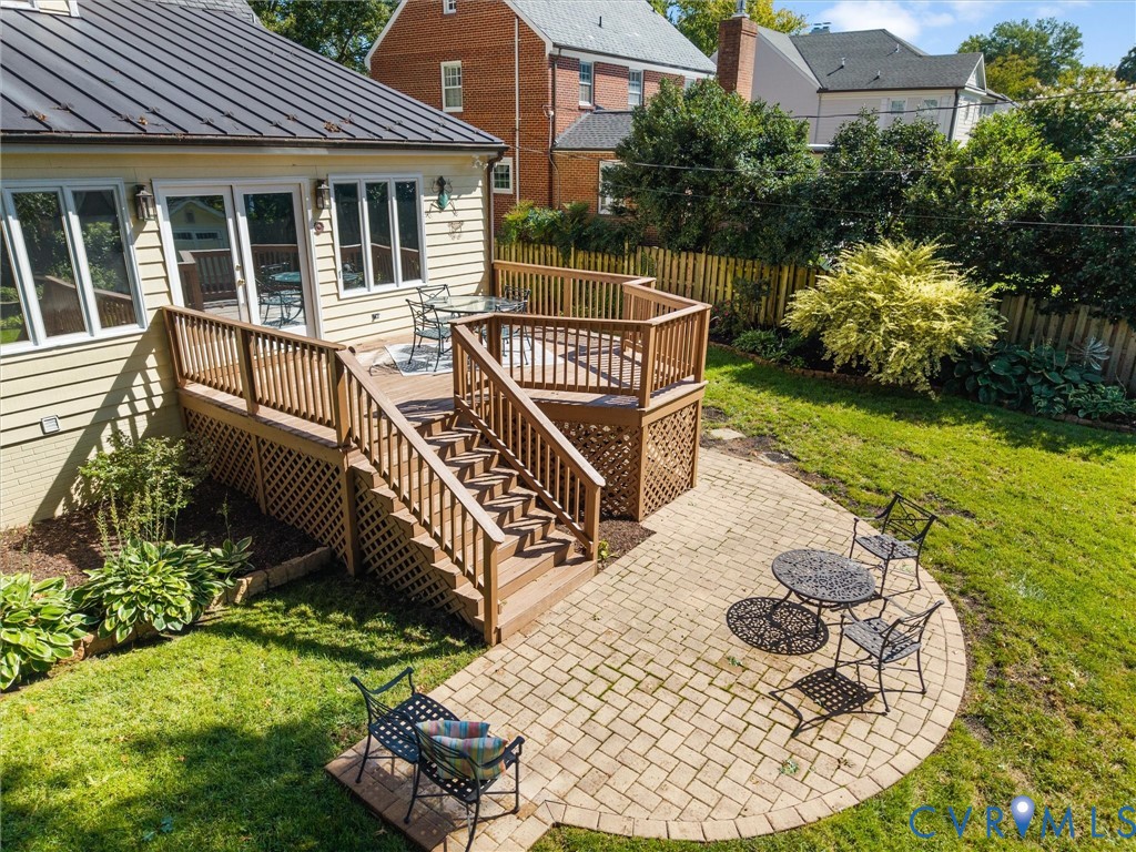 Expansive wood-finish deck with multiple levels, leading to a paver patio and green space