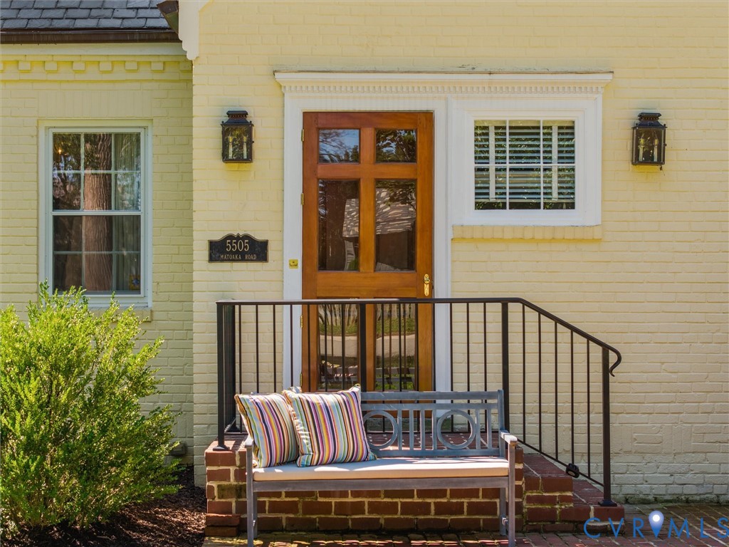 Yellow brick exterior with a wood entry door, white window trim, and two black wall-mounted lanterns