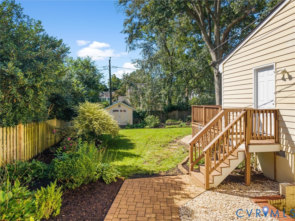 Expansive backyard featuring a manicured lawn, brick patio, wood fencing, and a separate storage shed