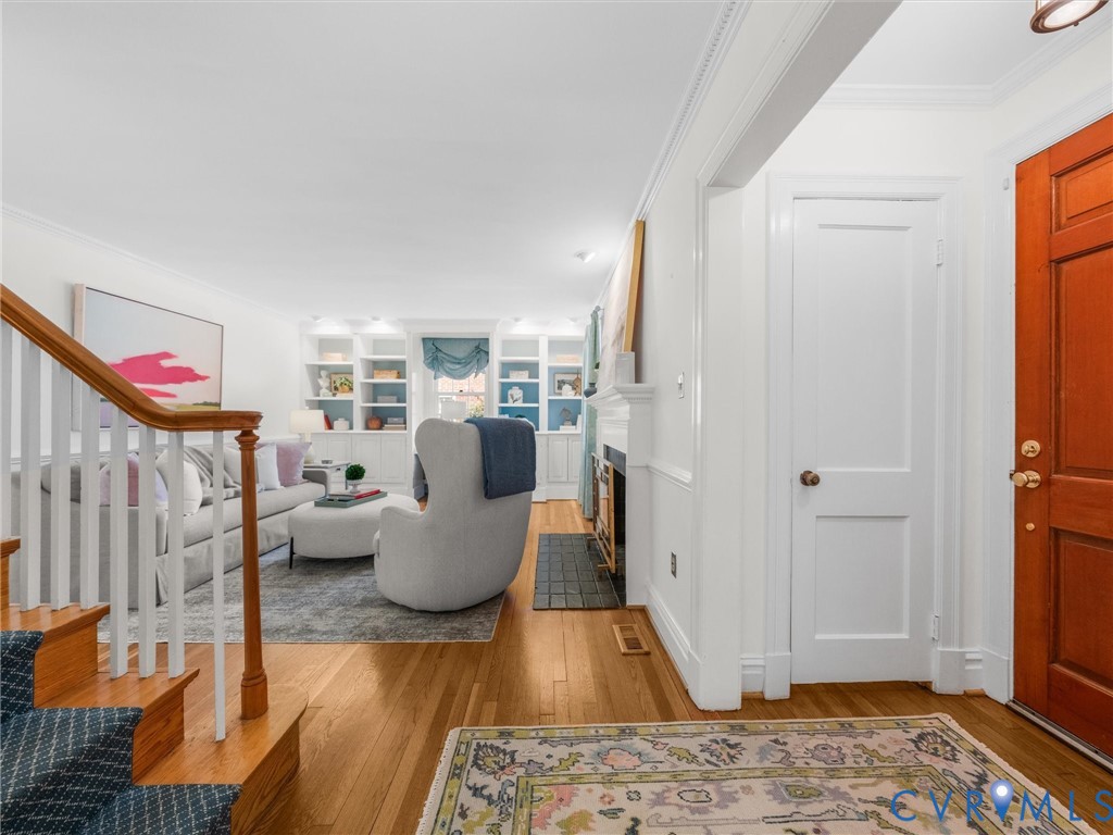 Hardwood flooring, custom built-in shelving, fireplace with hearth, staircase with wood handrail, and a paneled front door
