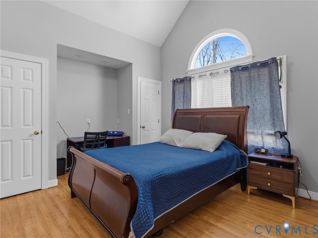 Vaulted ceiling with an arched window, wood-finish flooring, recessed lighting, and a built-in desk alcove