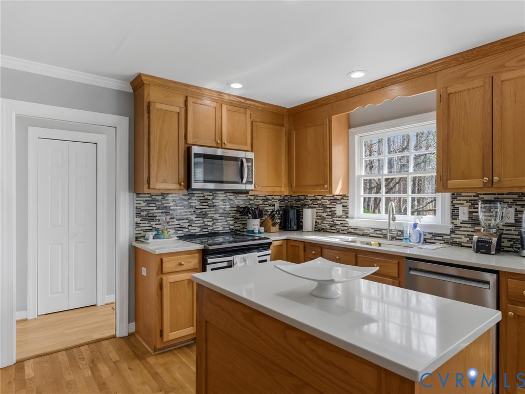 Kitchen with wood cabinetry, stainless steel appliances, mosaic tile backsplash, and light-toned countertops