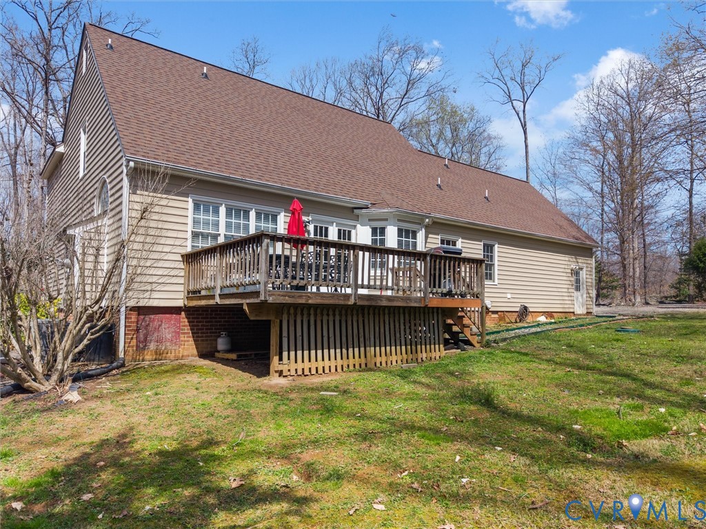 Expansive rear deck with wooden railing and stairs, multiple windows, and a side door entry