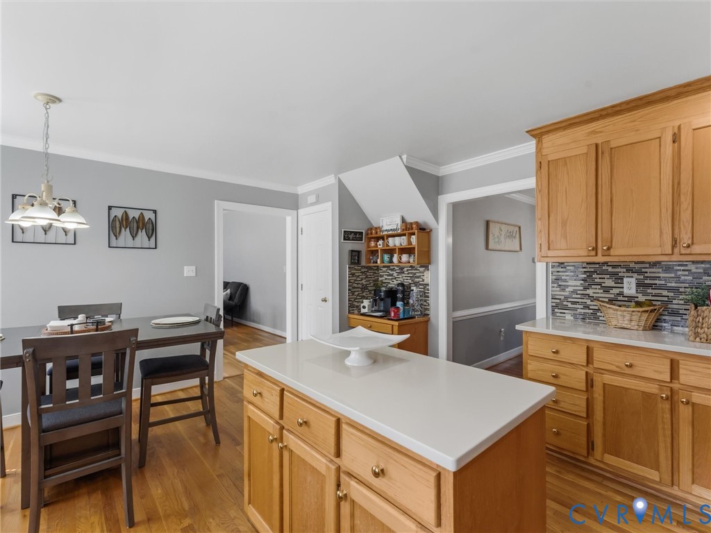 Open-concept kitchen and dining area featuring warm wood cabinetry, white quartz countertops, mosaic tile backsplash, a center island with prep space, and hardwood flooring throughout