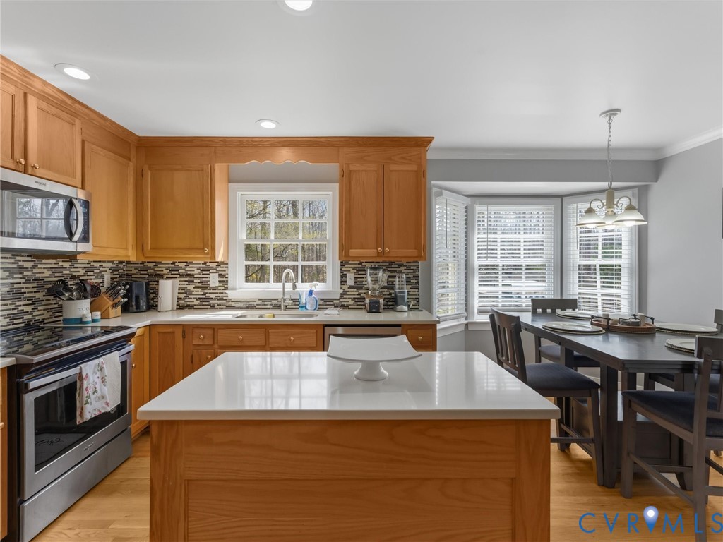Natural wood cabinetry, stainless steel appliances, mosaic tile backsplash, recessed lighting, and a bay window with blinds