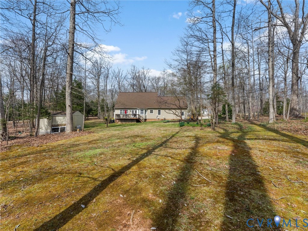 Expansive backyard featuring a deck, mature trees, and an accessory building