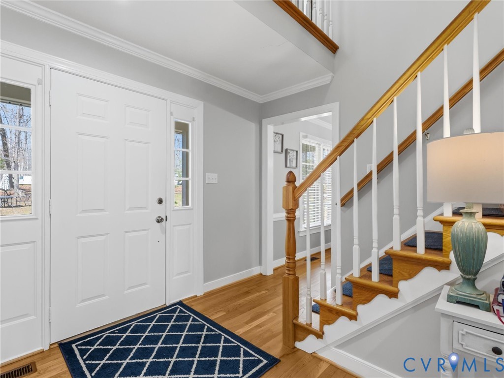 Hardwood flooring, painted white trim, staircase with wood handrail, paneled entry door, and side light windows Hardwood flooring, painted white trim, staircase with wood handrail, paneled entry door, and side light windows