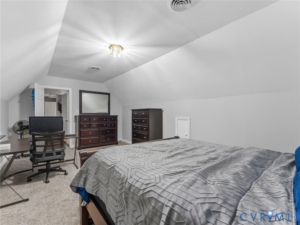 Carpeted flooring, vaulted ceiling with a flush-mount light fixture, and an attic access panel