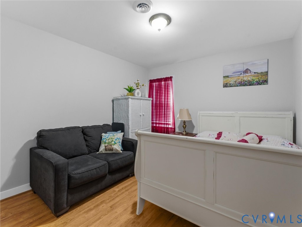 Versatile secondary bedroom or home office space featuring wood-finish flooring, a black upholstered loveseat, and white built-in cabinetry with panel detailing
