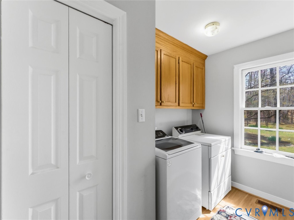 Integrated laundry area featuring wood-finish flooring, wood cabinetry, and a double-paned window
