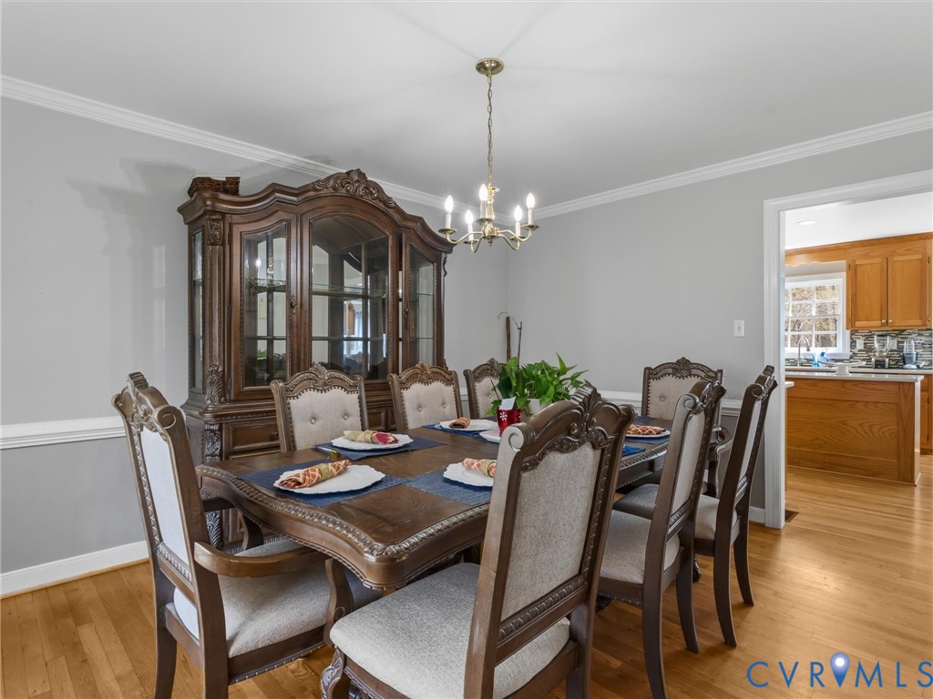 Hardwood flooring, crown molding, and a chandelier illuminate this dining space