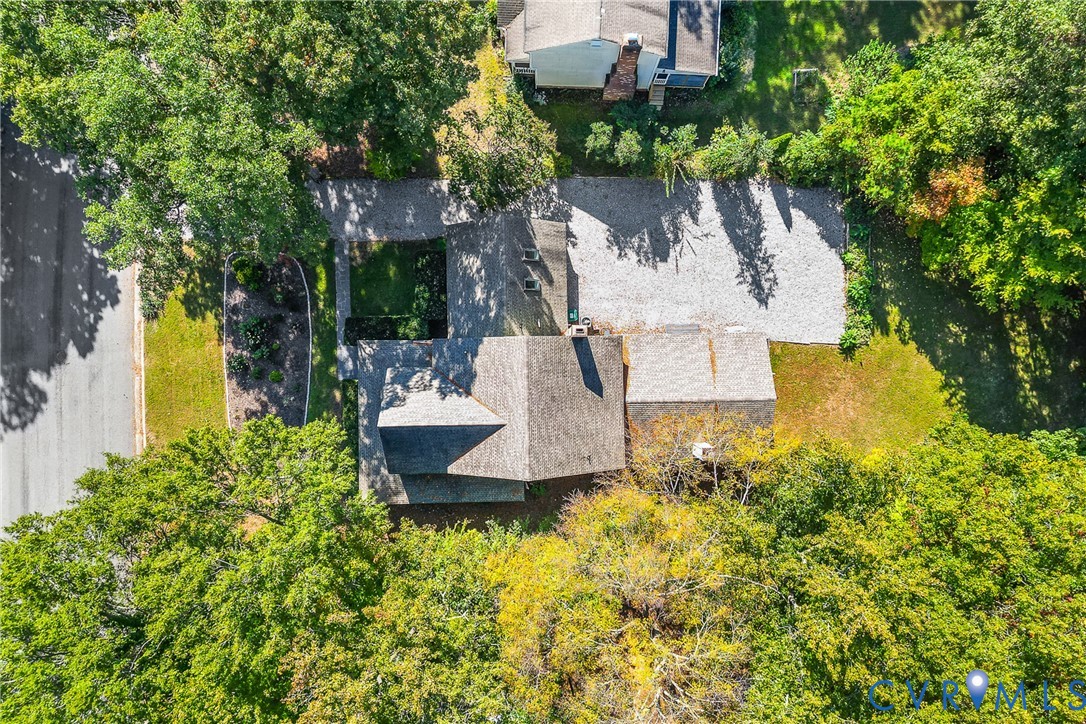 Aerial perspective of a detached residence featuring a shingled roof, a stone driveway, and established tree canopy