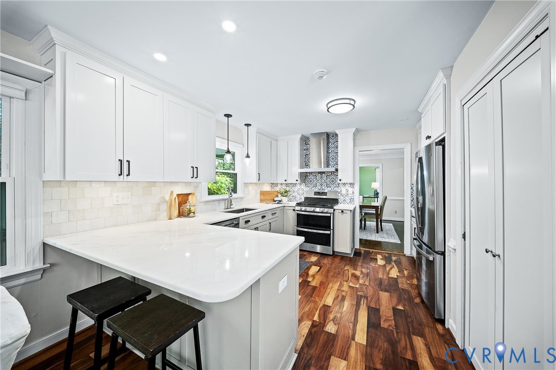 Kitchen featuring white shaker-style cabinetry, solid-surface countertops, subway tile backsplash, stainless steel appliances, and wood-finish flooring
