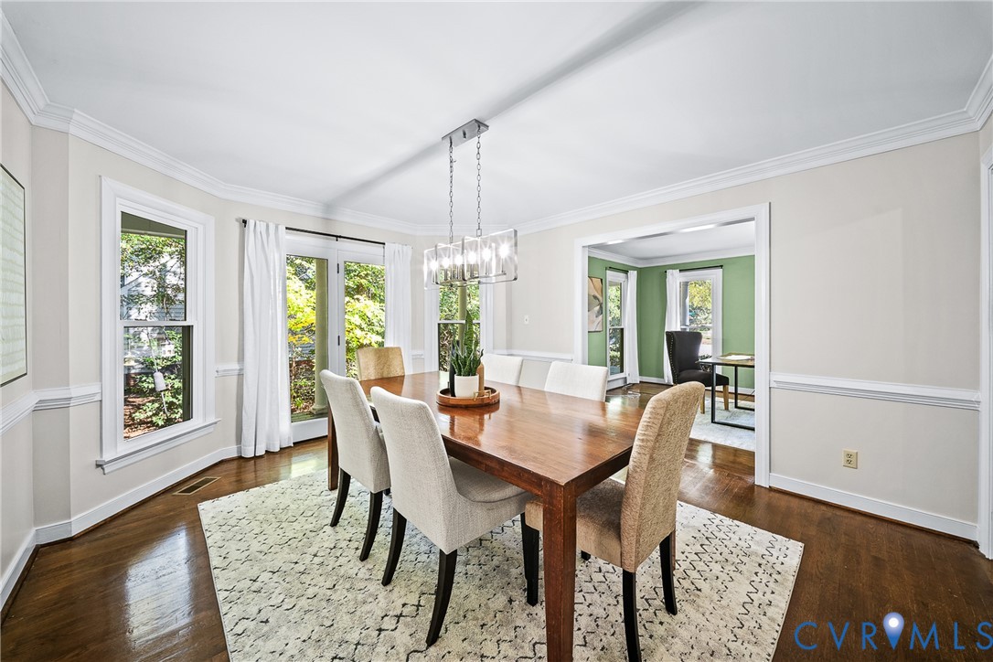 Dining area featuring wood-finish flooring, crown molding, chair rail trim, and a multi-light chandelier