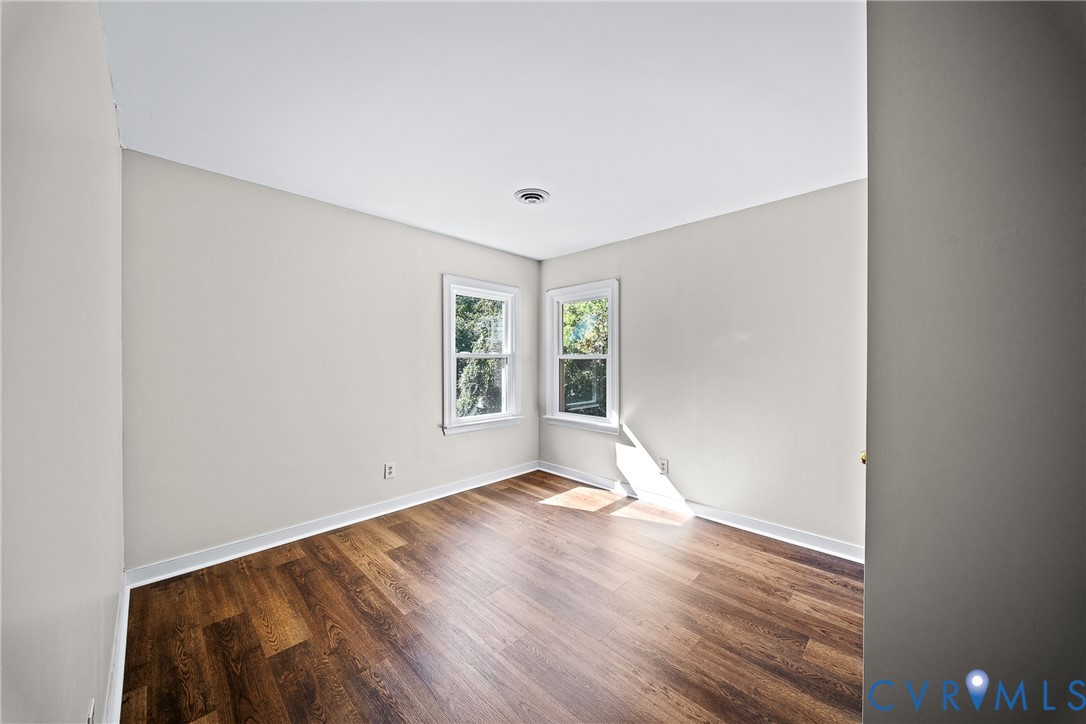 Interior room featuring neutral wall paint, wood-finish flooring, and two double-hung windows with white casings
