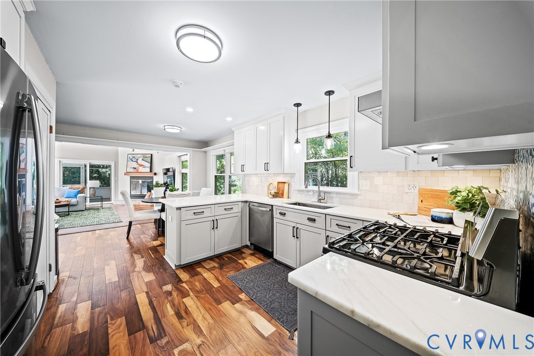 Kitchen featuring white shaker cabinetry, stainless steel appliances, light-toned stone countertops, a tiled backsplash, and wood-finish flooring