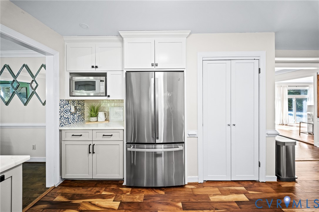 Kitchen featuring white cabinetry, stainless steel refrigerator, built-in microwave, patterned backsplash tile, and wood-finish flooring