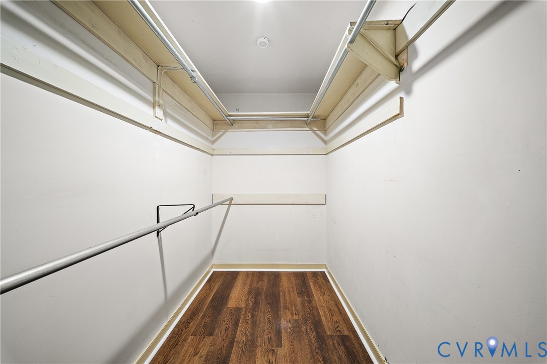 Walk-in closet featuring wood-finish flooring, tiered shelving, and dual-level metal hanging rods