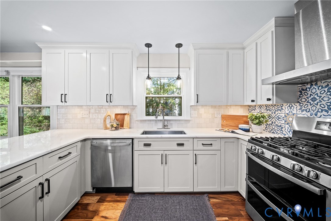 Kitchen featuring white shaker-style cabinetry, stainless steel appliances, solid surface countertops, patterned tile backsplash, and wood-finish flooring