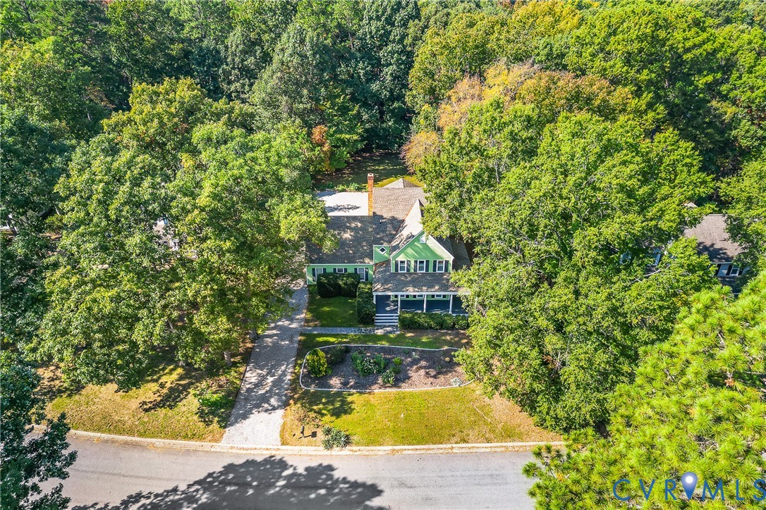 Two-story home with a covered front porch, light-toned exterior siding, asphalt shingle roof, long concrete driveway, and mature landscaping on a wooded lot
