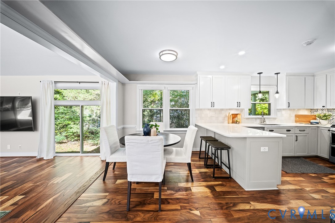Kitchen featuring white cabinetry, wood-finish flooring, a quartz-topped peninsula with bar seating, and sliding glass doors