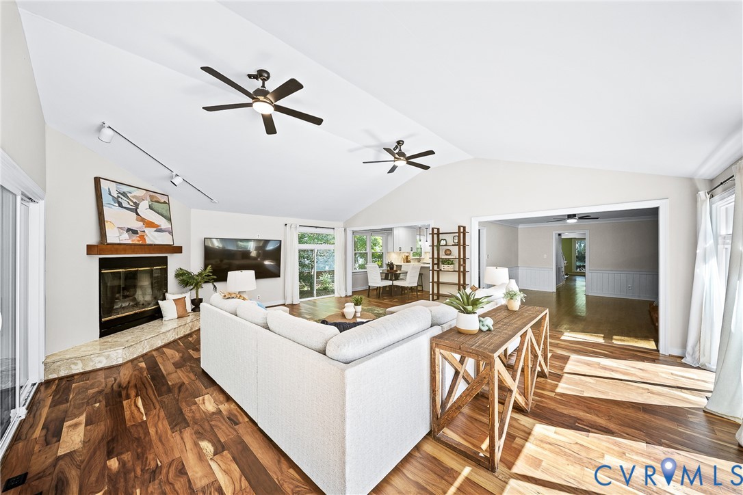 Vaulted ceilings, wood-finish flooring, stone-surround fireplace with a timber mantel, recessed track lighting, and two ceiling fans